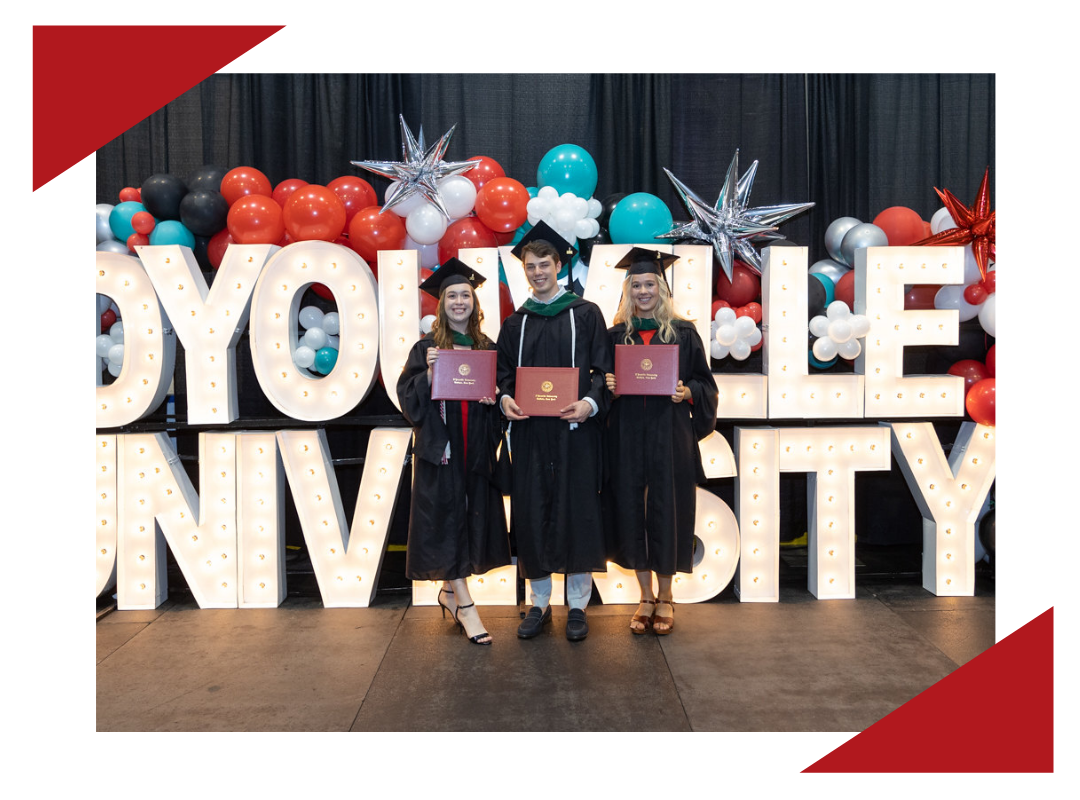 DYU graduates in cap and gown standing on stage.